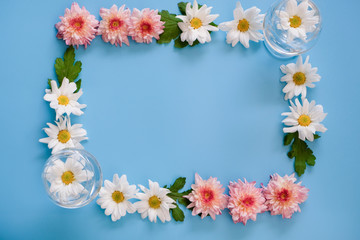 Top View or bird's eye view, background concept, a group of pink and white flowers that arranged on the edge of picture on blue background. there are two clear glasses on the corner