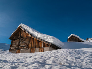 Snow-covered wooden house in the high mountains, in the dolomites