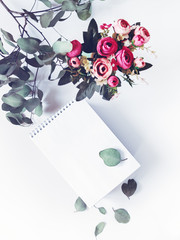 The concept of business planning, study, freelance, diary. An open notebook with blank pages is on a white background. Nearby is a branch of eucalyptus and flowers. Flat lay.