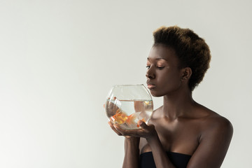 attractive african american girl holding aquarium with fish isolated on grey