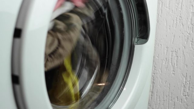 Rising view of a washing machine spinning a load of mixed colours clothes and then stopping