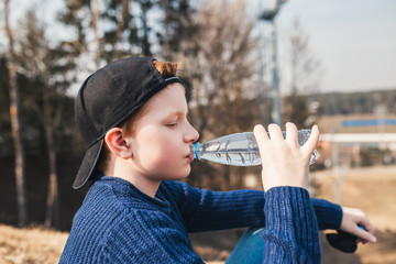 A boy drinks water from a plastic bottle - quenching thirst on a camping trip - hiking