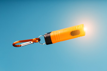 An orange led flashlight with a carabiner glows on a blue background.