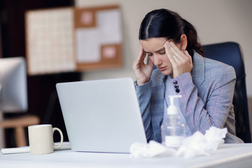 Sick, ill unhealthy female employee working in workplace in office and wearing surgical hygienic mask on her face. Concept of corona virus or covid-19