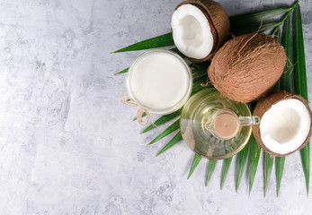 Obraz na płótnie Canvas coconuts, palm leaves and coconut oil on a gray background