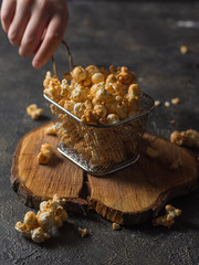 Popcorn in a metal basket and next to it scattered with a hand on a dark background and a wooden...