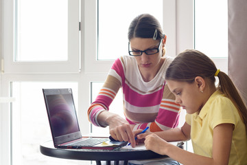A home tutor teaches a child sitting at a table and using a computer