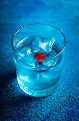 Blue old fashioned cocktail with cherry on the rustic background. Selective focus. Shallow depth of field.