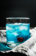 Blue old fashioned cocktail with cherry on the rustic background. Selective focus. Shallow depth of field.