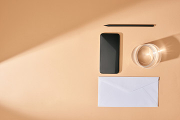 flat lay with smartphone, pencil, glass of water and envelope on beige background