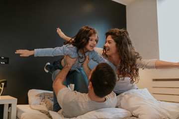 Photo of young happy family enjoying time together. Father is holding daughter while she imitating plane with her mother.