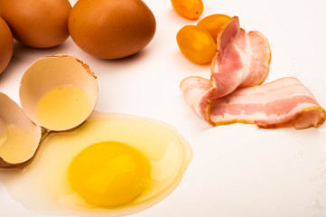 Broken chicken egg, bacon slices, tomatoes and chicken eggs on a white background. Close up.
