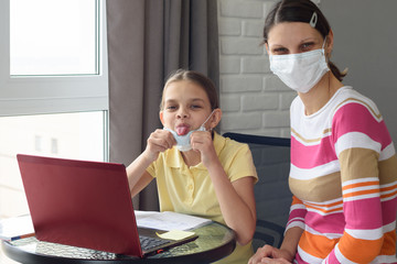 The girl took off her medical mask and showed her tongue, doing homework in self-isolation mode
