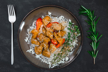 Tasty chicken with rice on brown plate on black background.