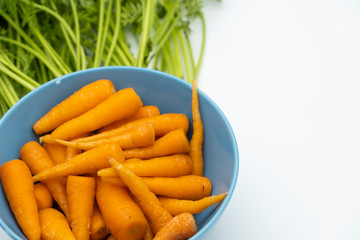 Fresh baby carrots in the blue bowl with green leaves on background, vegetable food concept