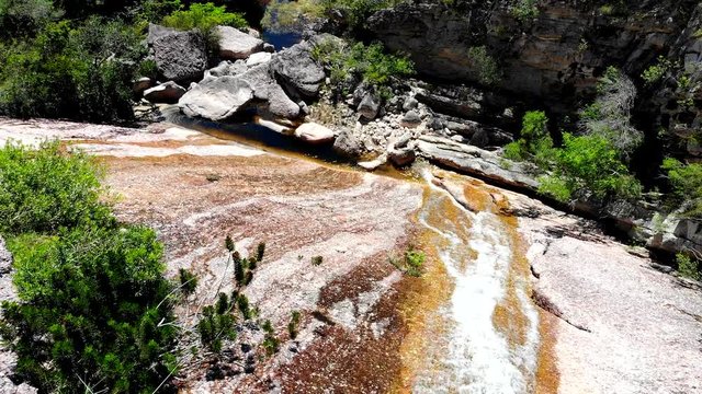 Aerial shot of flowing water at Conceicao dos gatos waterfall, Chapada Diamantina, Bahia, Brazil. Drone moving forward and following water flow.
