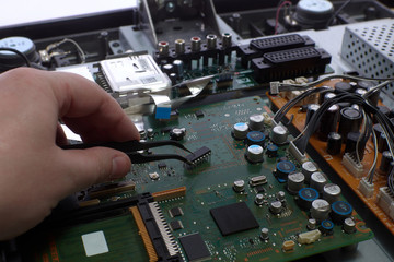 Man's hand holds a chip with tweezers. Electronics repair. Disassembled LCD TV. Radio electronic...