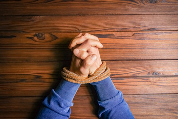 Hands tied with a rope life-threatening on a wooden background. Slavery in business is human abuse.