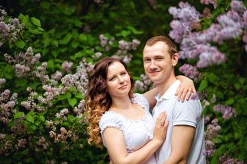 Romantic holidays for a guy and a girl in a spring park. Meeting a young couple in a lilac garden. Photo session in nature.
