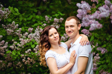 Fototapeta premium Romantic holidays for a guy and a girl in a spring park. Meeting a young couple in a lilac garden. Photo session in nature.