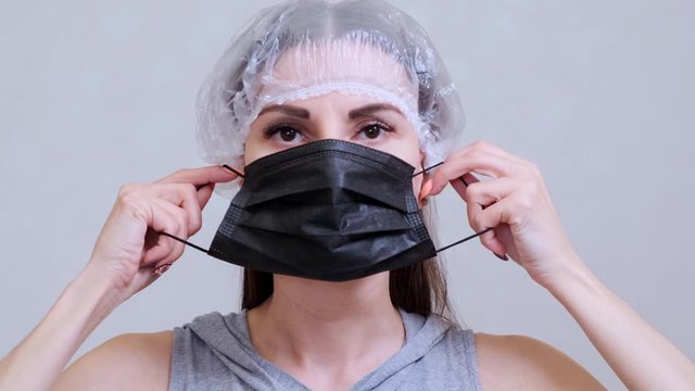Female patient in a disposable cap puts on a black protective mask. Hygiene concept. prevent the spread of germs and bacteria and avoid infection with the crown virus