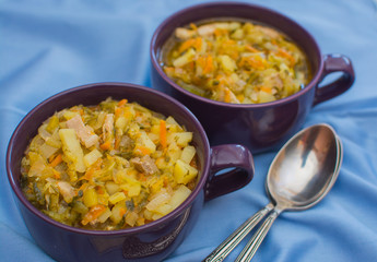 Traditional Russian sauerkraut soup in a purple porcelain cup on a blue napkin.