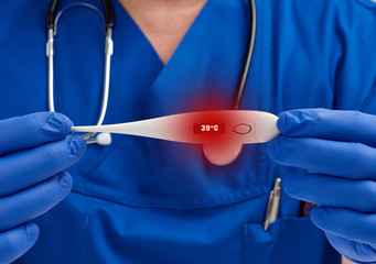 doctor sitting in blue uniform and latex gloves holds a white electronic thermometer, doctor’s office, on the thermometer the display shows an elevated temperature of 39 degrees Celsius