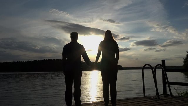 ein verliebtes Paar am See bei Sonnenuntergang halten H&auml;ndchen