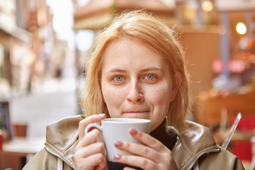 White female tourist drinks coffee in street cafe.