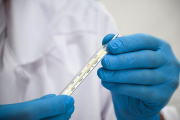 Closeup doctor hands in blue rubber gloves holding a mercury thermometer, on white background (selective focus)