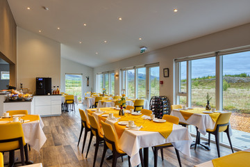 Elegant and minimalist restaurant in a Scandinavian hotel with fantastic views. Yellow and white tablecloths with breakfast cutlery. Large windows. Buffet, coffee and wines