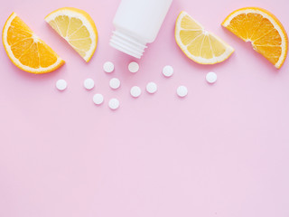 scattered vitamin pills and bottle with lemon orange on pink background. Copyspace, flat lay. Concept boost immune system, medicine and tablets.