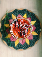 Homemade dried tomatoes in a glass jar with fresh herbs. Wooden background. Top view.