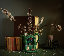 Still life with flowering apricot branches, books and an extinguished candle. Vintage.