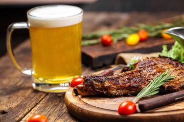  Juicy grilled meat on a wooden board with vegetables, herbs and a beer, side view, horizontal, closeup