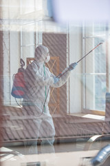 Coronavirus Pandemic. A disinfector in a protective suit and mask sprays disinfectants in house or...