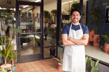 Portrait Of Smiling Male Owner Of Florists Standing In Doorway Surrounded By Plants