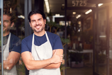 Portrait Of Smiling Male Owner Of Florists Standing In Doorway Surrounded By Plants