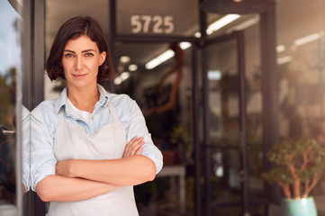 Portrait Of Smiling Female Owner Of Florists Standing In Doorway Surrounded By Plants