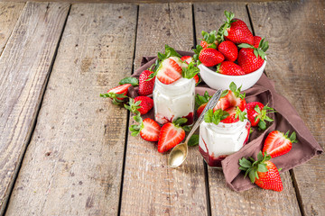 Sweet healthy yogurt with strawberry and strawberry jam in small portioned jars on wooden rustic table, copy space