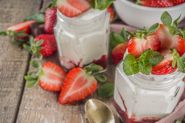 Sweet healthy yogurt with strawberry and strawberry jam in small portioned jars on wooden rustic table, copy space