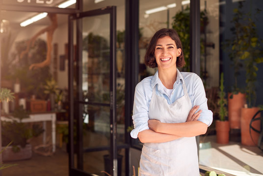 Portrait Of Smiling Female Owner Of Florists Standing In Doorway Surrounded By Plants