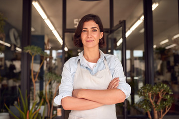 Portrait Of Smiling Female Owner Of Florists Standing In Doorway Surrounded By Plants