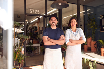 Portrait Of Smiling Male And Female Owners Of Florists Standing In Doorway Surrounded By Plants