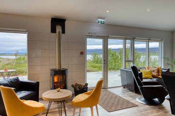 Elegant and minimalist restaurant in a Scandinavian hotel with fantastic views of the countryside and mountains. Yellow and white tablecloths. Large windows, wood-burning stove and leather sofas