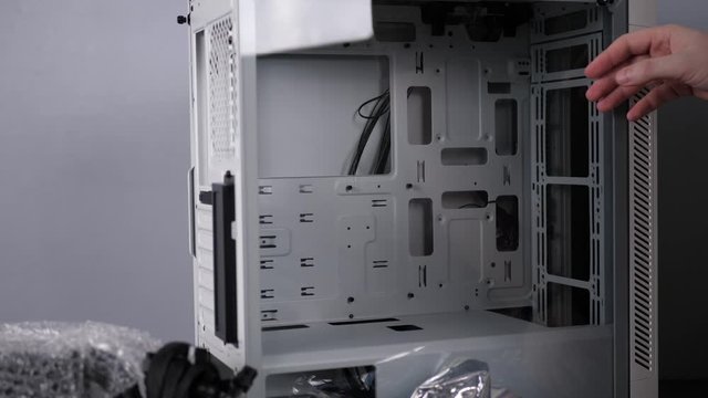 Engineer man assemblies desktop PC in white computer case, male technician removes the glass side cover midi-tower.
