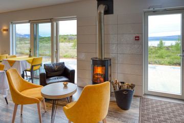 Elegant and minimalist restaurant in a Scandinavian hotel with fantastic views of the countryside and mountains. Yellow and white tablecloths. Large windows, wood-burning stove and leather sofa