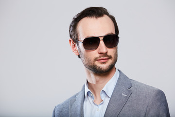 Elegant young handsome man in sunglassesand in stylish gray jacket. Studio fashion portrait.