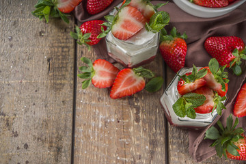 Sweet healthy yogurt with strawberry and strawberry jam in small portioned jars on wooden rustic table, copy space