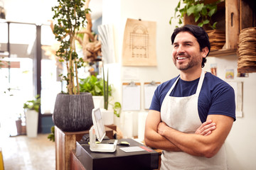 Smiling Male Sales Assistant Standing By Sales Desk Of Florists Store